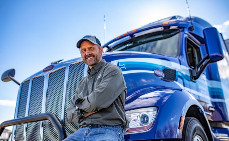 Marten driver sitting on front bumper of blue Marten truck