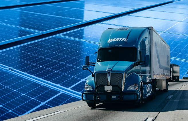Marten truck and trailer driving on road with solar panels in background representing innovation.