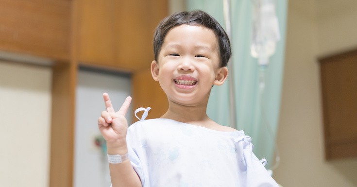 Little boy smiling and holding peace sign.